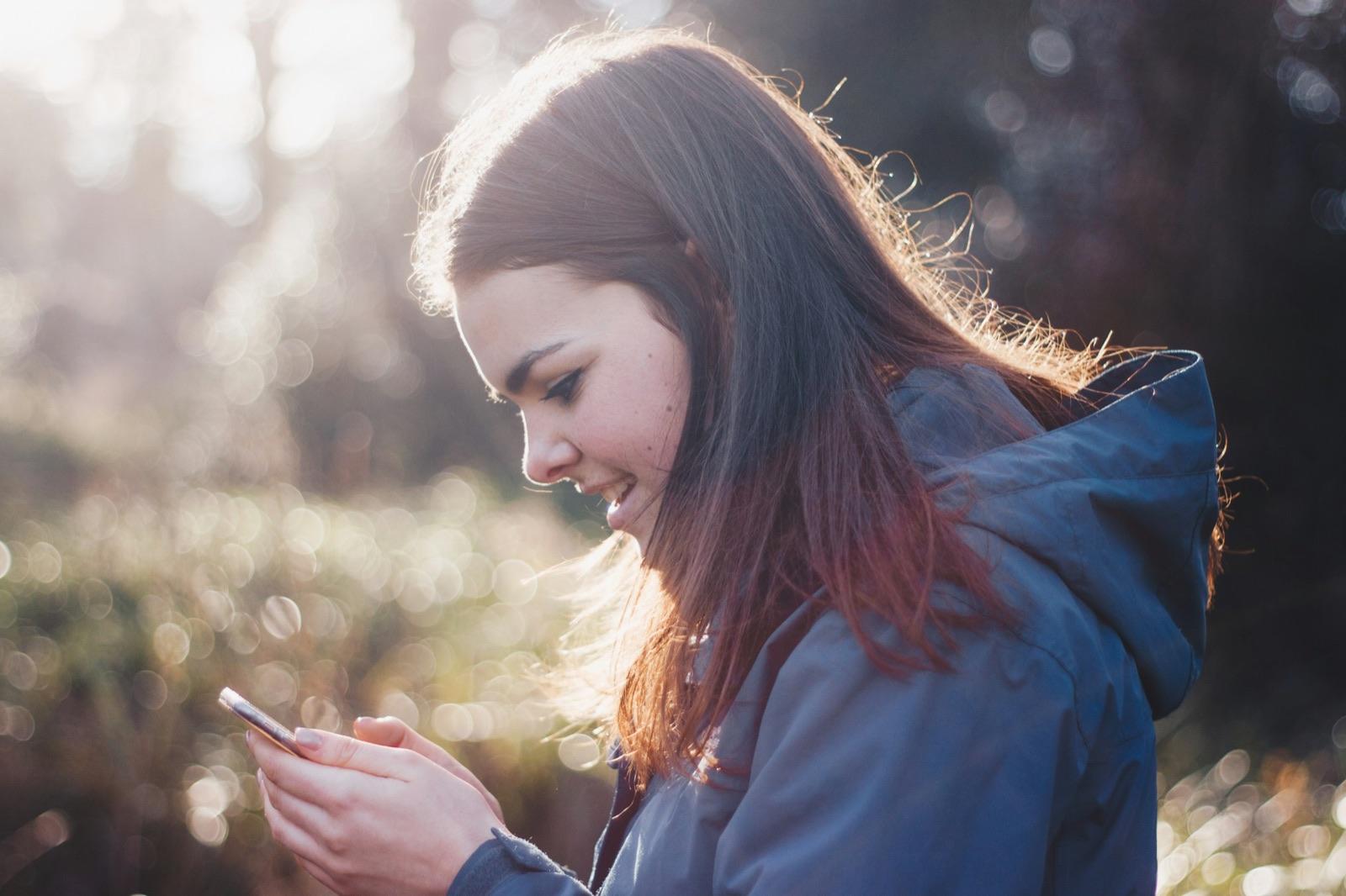 A woman outdoors in the evening light, glancing at her phone